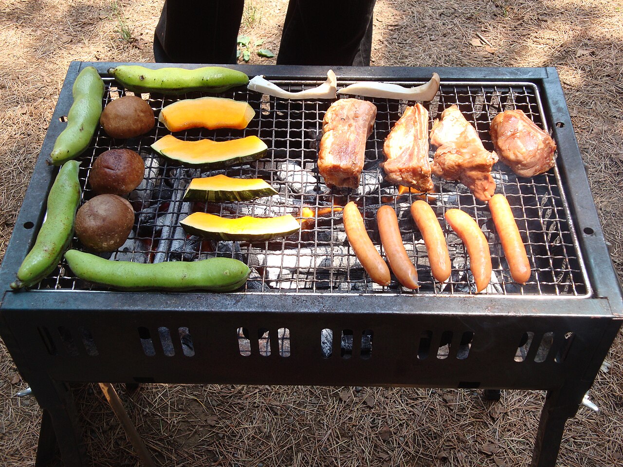 Una barbacoa de carbón con verduras, carne y salchichas sobre la parrilla